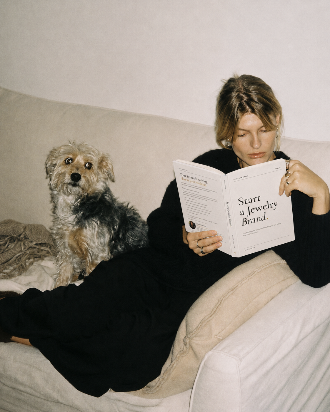 Woman reading Start A Jewelry Brand on a sofa beside her dog
